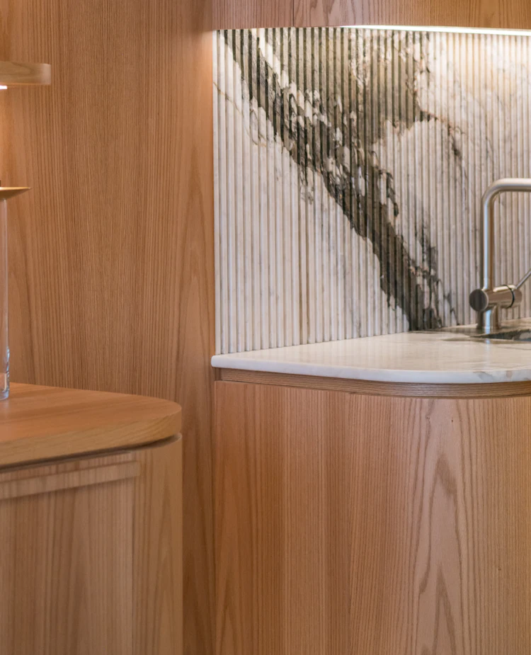 A curved timber kitchen bench beneath a fluted marble splashback